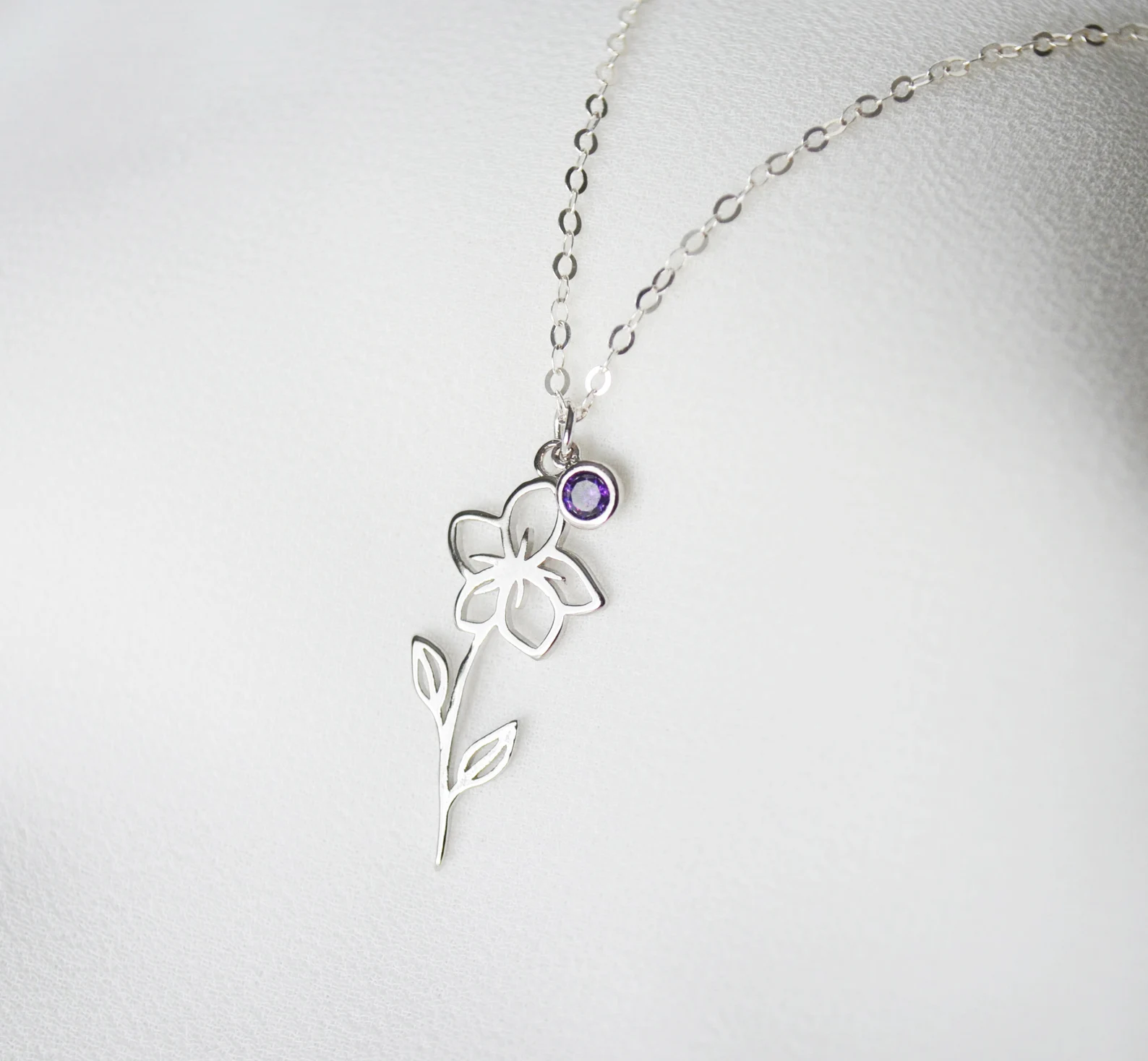 A sterling silver chain necklace with a cutout violet flower pendant and a tiny round amethyst birthstone charm, a delicate February birthday gift idea.