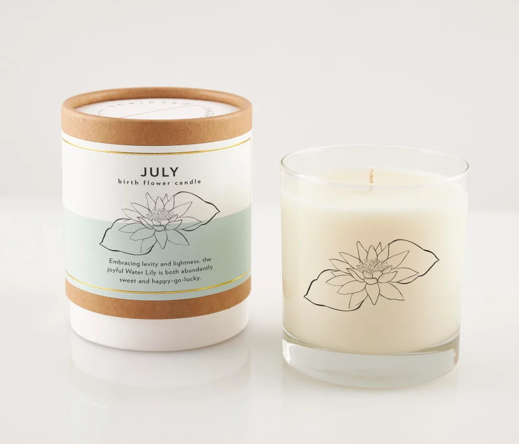 A July birth flower soy candle in a glass vessel etched with a water lily illustration beside its kraft tube gift box, an elegant July birthday gift idea.