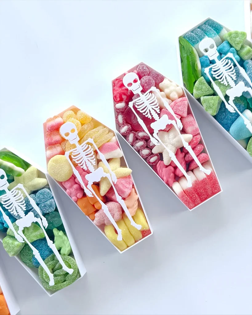 Coffin-shaped candy tins filled with colorful sour gummies and a skeleton topper, spooky and sweet Halloween party favors.