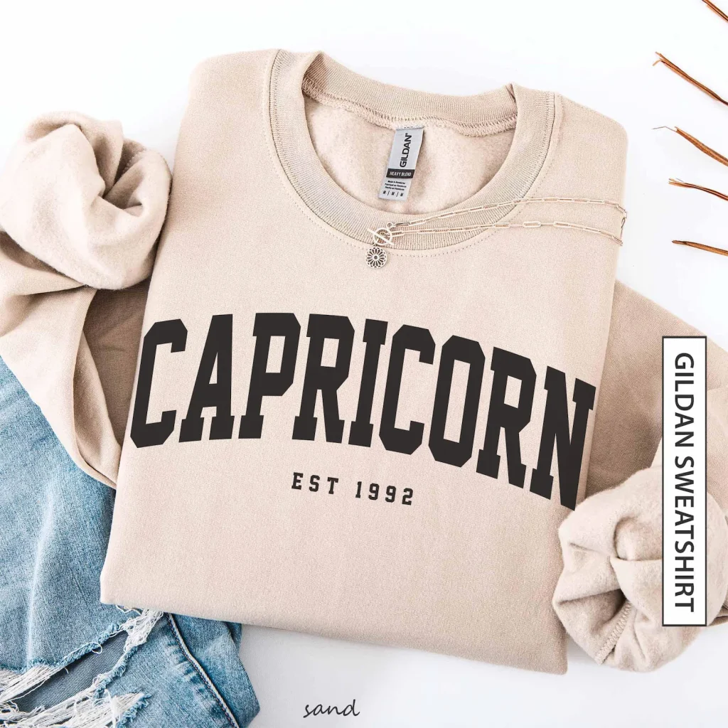 A sand coloured Capricorn sweatshirt with a personalised birth year, a casual and cosy December birthday gift idea.