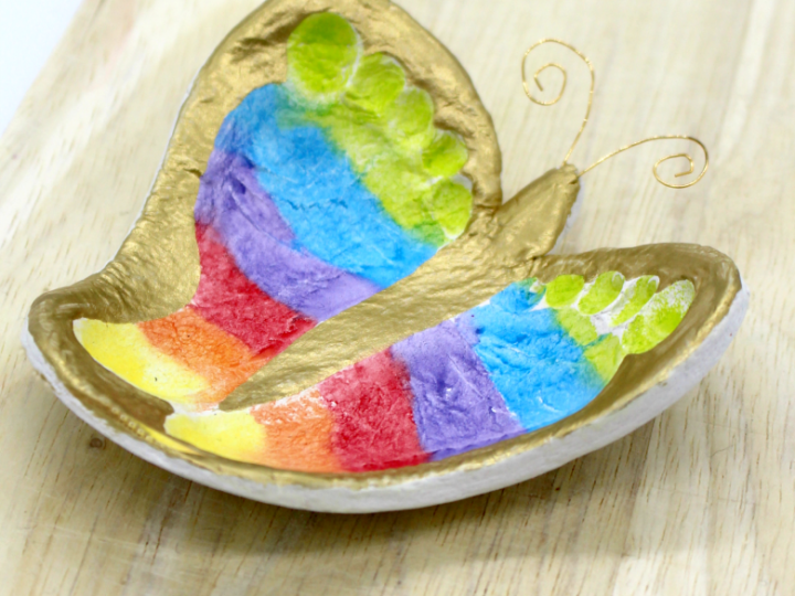 A gold-painted clay dish featuring a colorful rainbow footprint, a sweet homemade gift for grandparents to treasure.