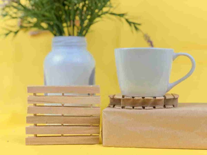 Two handcrafted popsicle stick coasters, one square, one round, styled with a white mug and vase, making charming homemade gifts for grandparents.