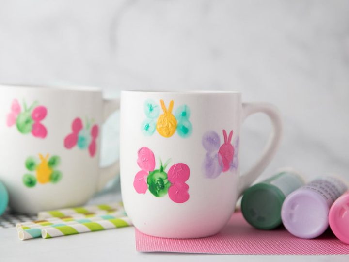 A white ceramic mug decorated with colorful thumbprint butterflies, an adorable and useful homemade gift for grandparents.