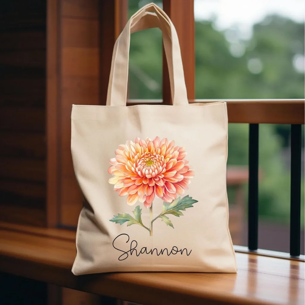 A personalized cream canvas tote bag featuring a watercolor orange chrysanthemum birth flower illustration, a practical and thoughtful November birthday gift idea.