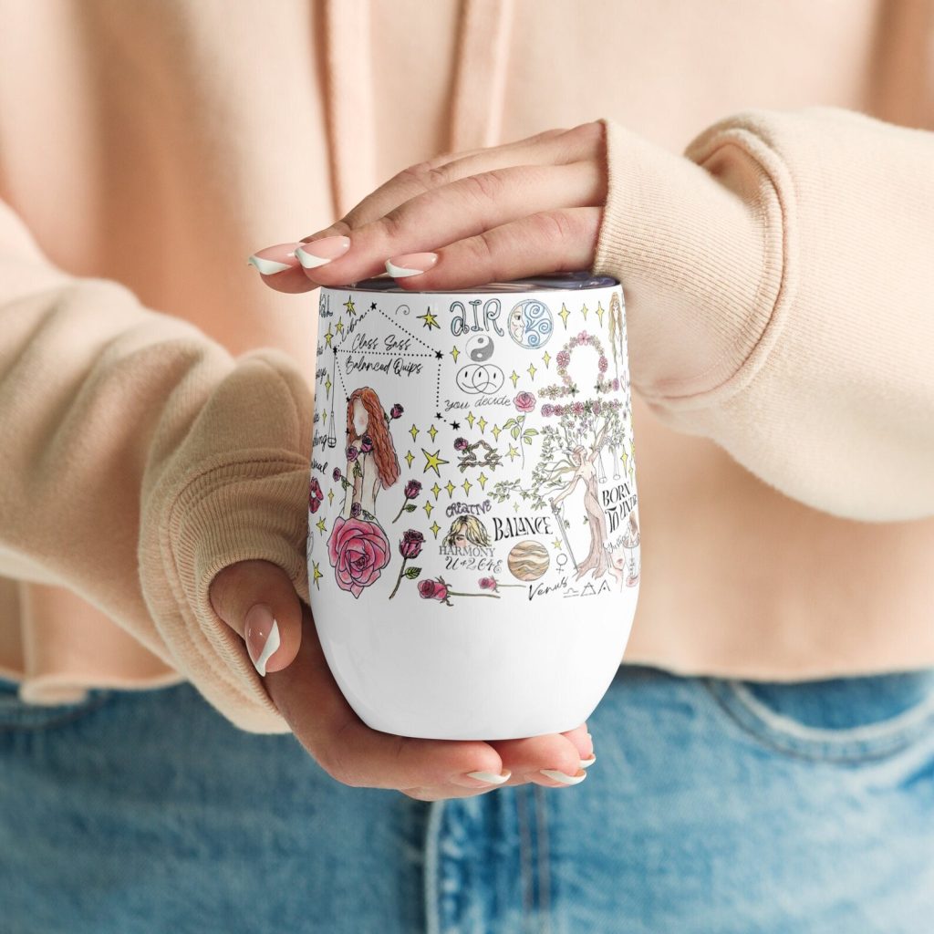 A woman holding a white insulated tumbler covered in colorful Libra zodiac illustrations and floral designs, fun October birthday gift ideas.