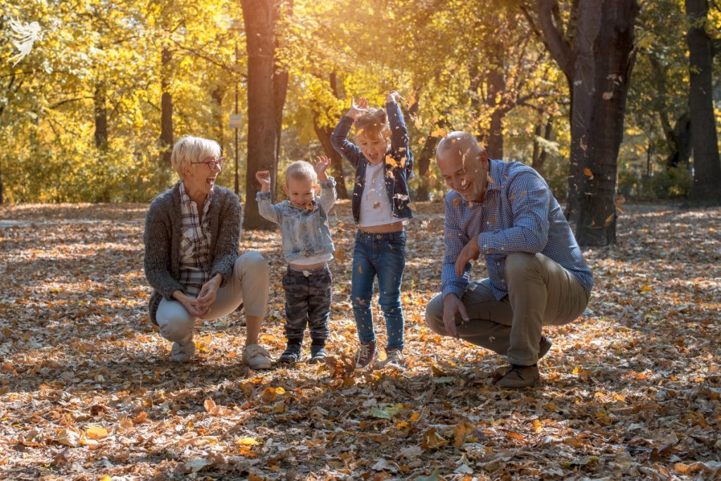 grandma and grandpa with their grandchildren playing in fall leaves for grandparents day