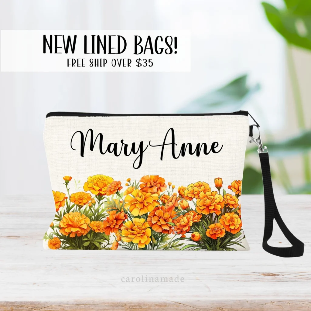 A personalized cream linen makeup bag printed with a vibrant orange marigold garden design and wrist strap, a practical October birthday gift idea.