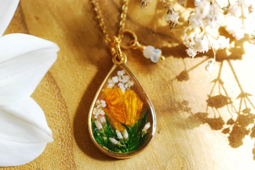 A gold teardrop resin pendant necklace encasing a real dried marigold flower and green moss, a unique among October birthday gift ideas.