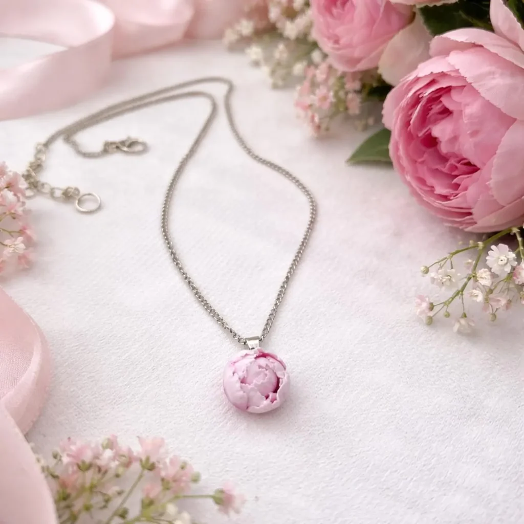 A delicate silver chain necklace featuring a handcrafted pink peony flower pendant surrounded by fresh roses and baby's breath, a romantic November birthday gift idea.