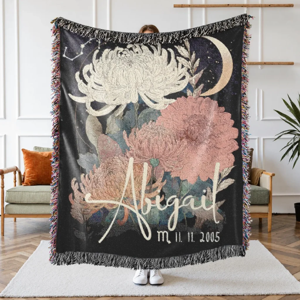A person holding a large personalized woven throw blanket featuring chrysanthemum and peony florals on a dark celestial background, among the most memorable November birthday gift ideas.