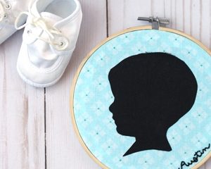 A delicate embroidered child silhouette on a round hoop with a light blue background, an elegant homemade gift for grandparents.