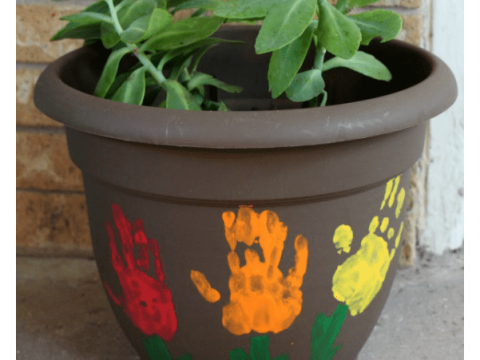 A gray flower pot painted with colorful children's handprints growing into flowers, a heartfelt homemade gift for grandparents.