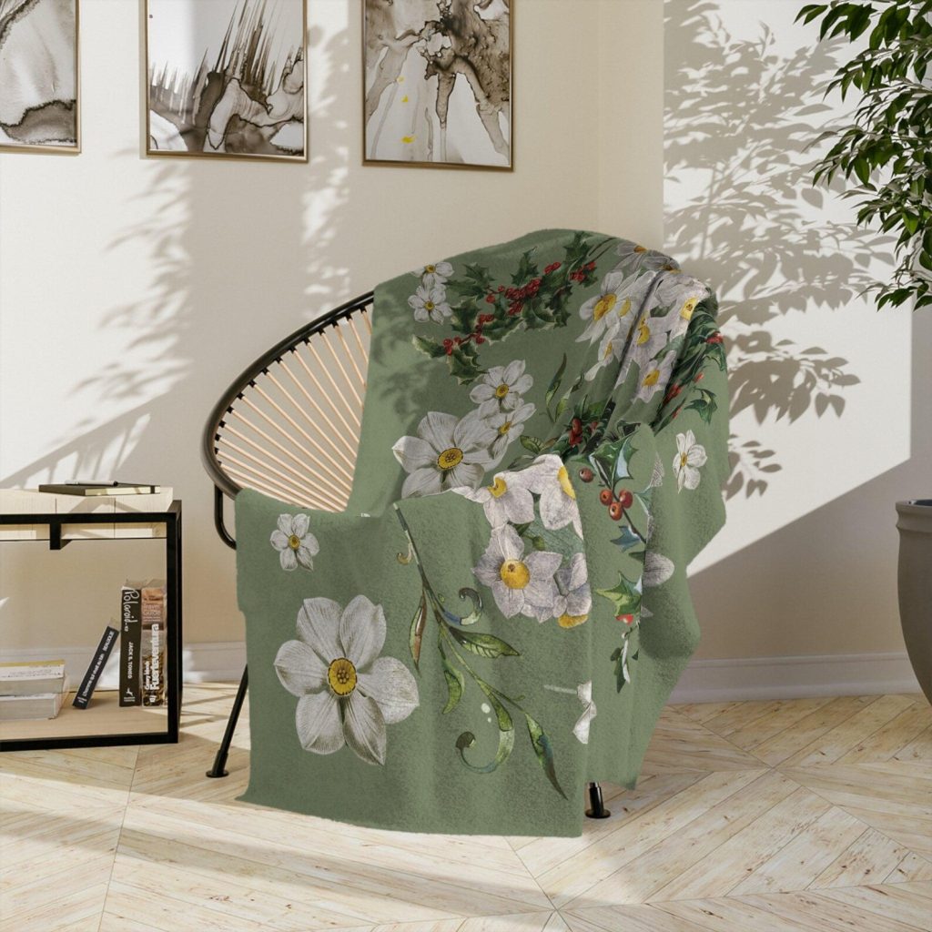 A sage green throw blanket printed with narcissus and holly birth flowers, a cozy and gorgeous December birthday gift idea.