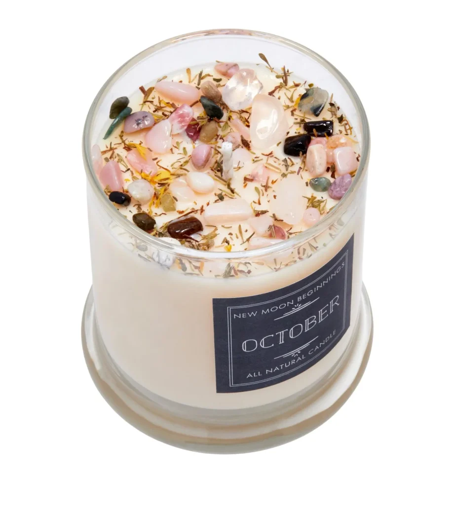 A white soy candle topped with colorful gemstone chips and dried botanicals in a glass jar, a luxurious and unique October birthday gift idea.