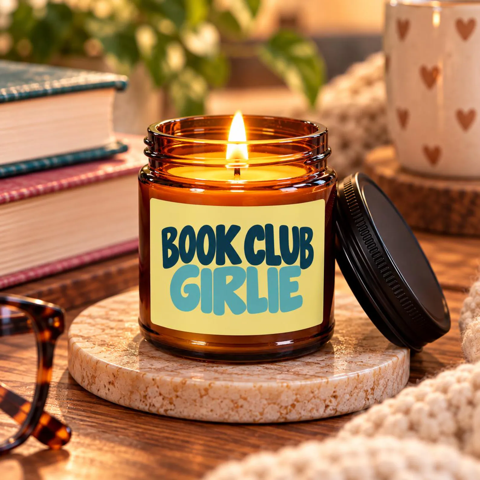 Lit amber jar Book Club Girlie candle beside reading glasses and stacked books on a cozy desk, a fun and relatable book club squad gifts she will adore.