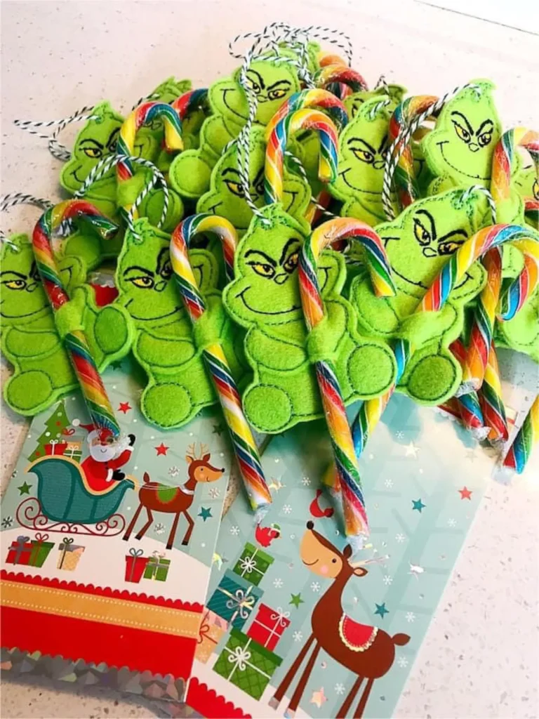Green felt Grinch face candy cane holders filled with rainbow candy canes on festive Christmas gift bags, irresistibly cute and affordable Grinch party favor ideas for kids.