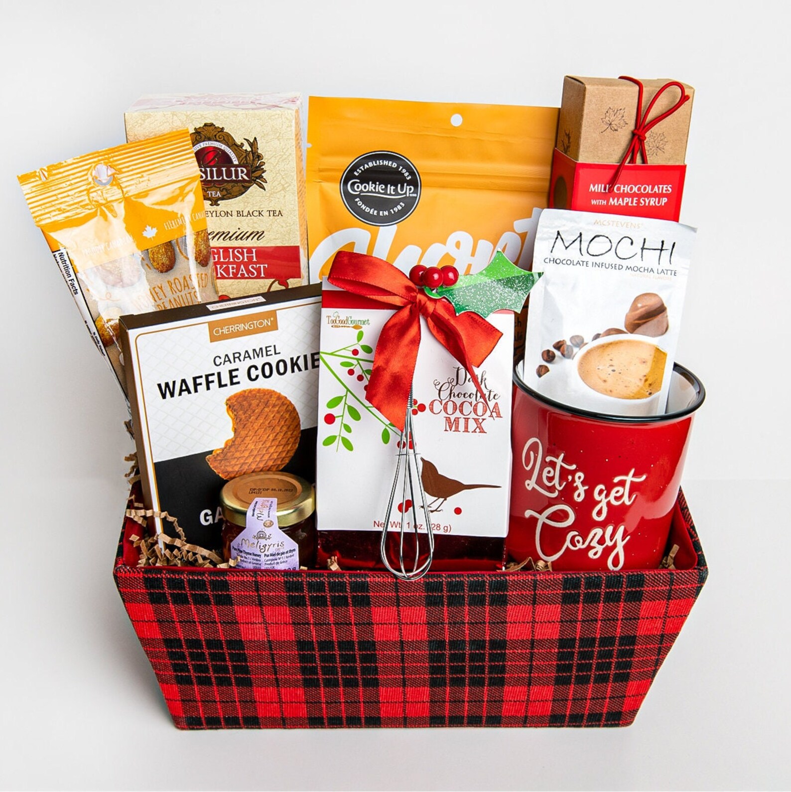 Red buffalo plaid basket packed with caramel waffle cookies, dark chocolate cocoa mix, Ceylon tea, mochi latte, maple chocolates and a Letโs Get Cozy mug, a generously filled Christmas hostess gift ideas perfect for the one who loves cozy winter treats.