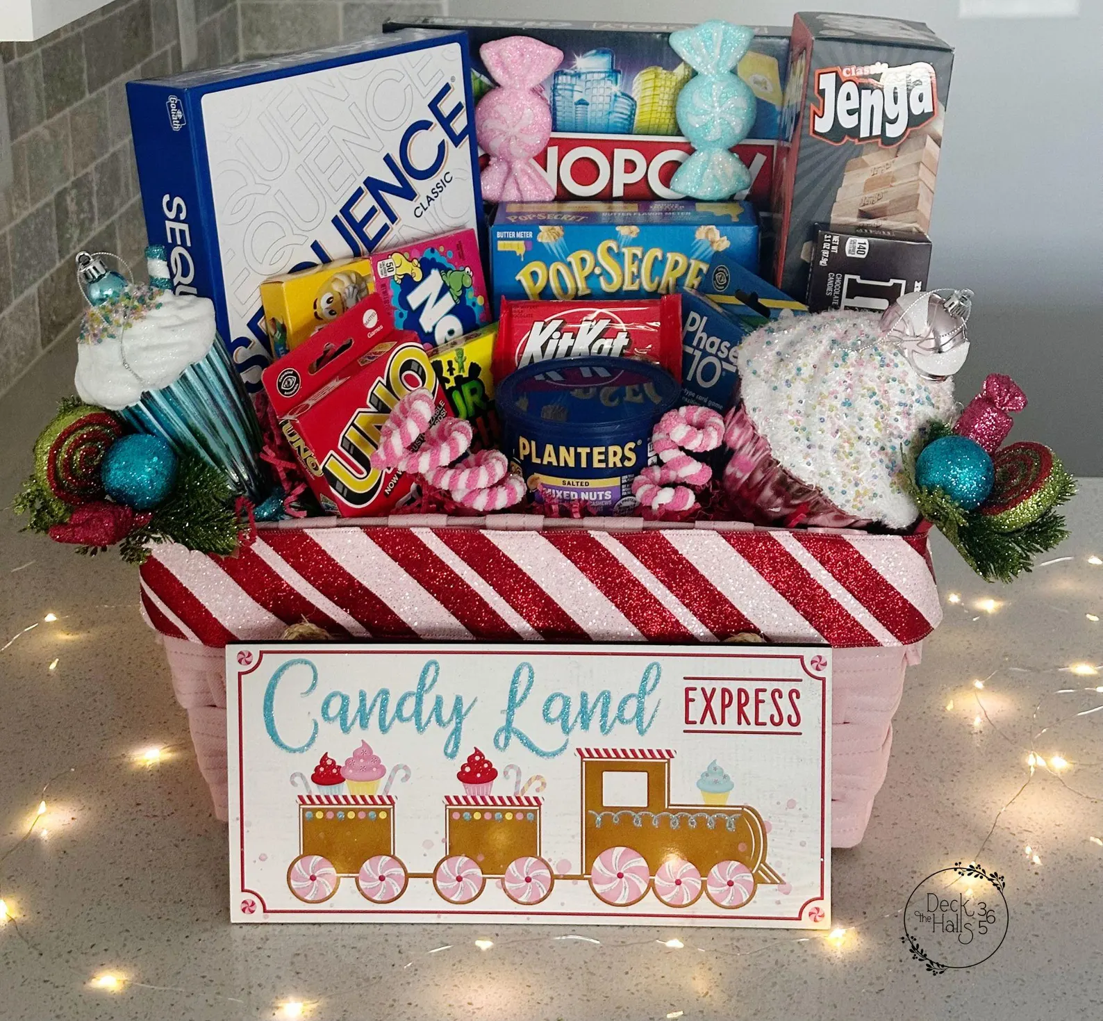 Candy Land Express themed Christmas gift basket packed with Sequence, Monopoly, Jenga, Uno, Phase 10, KitKat, Planters nuts and popcorn in a candy cane striped basket, the ultimate and irresistible gift for the board game loving family who loves snacking while they play.