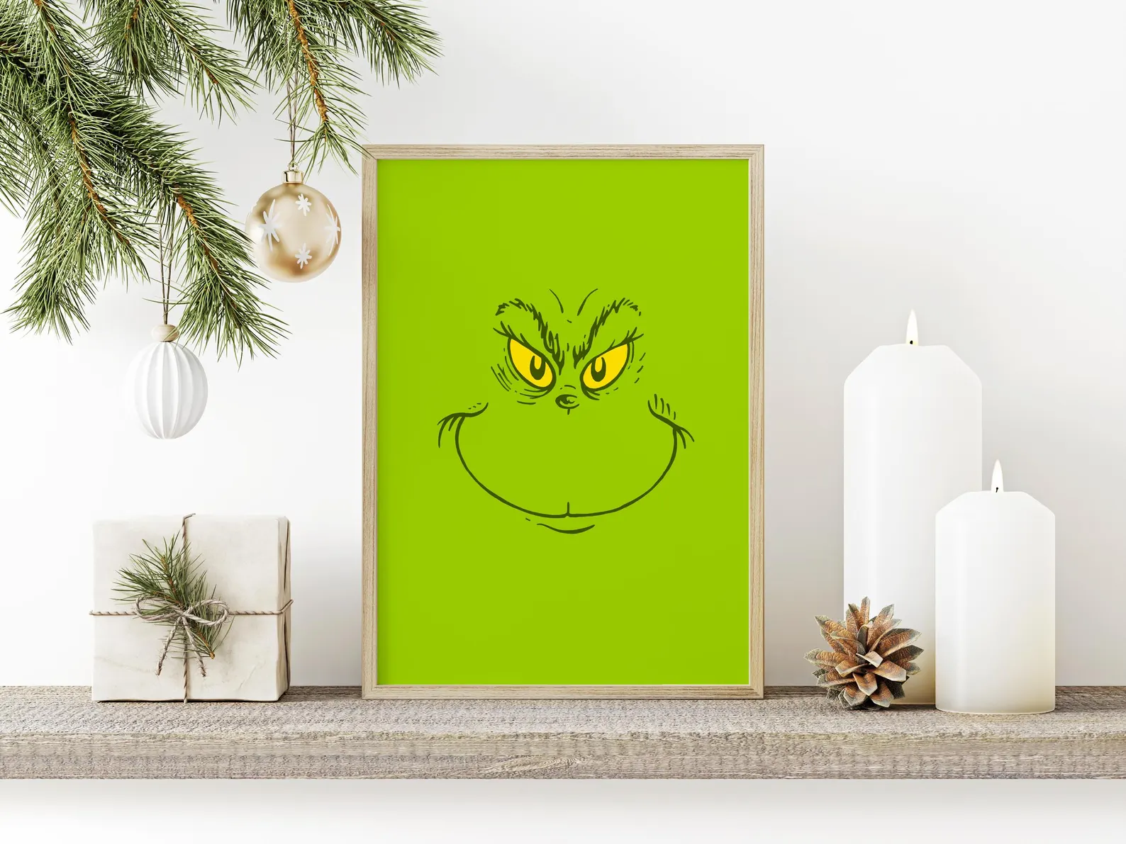 Bold green Grinch face framed wall art print with glowing yellow eyes displayed on a festive mantel, an iconic and eye catching Grinch party decor statement piece.