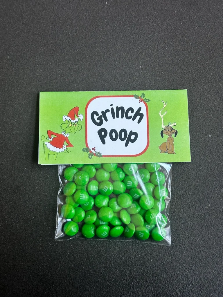 Bag of green M&Ms topped with a funny Grinch Poop label featuring the Grinch and Max dog, a cheeky and laugh out loud Grinch party candy favor kids and adults will enjoy.